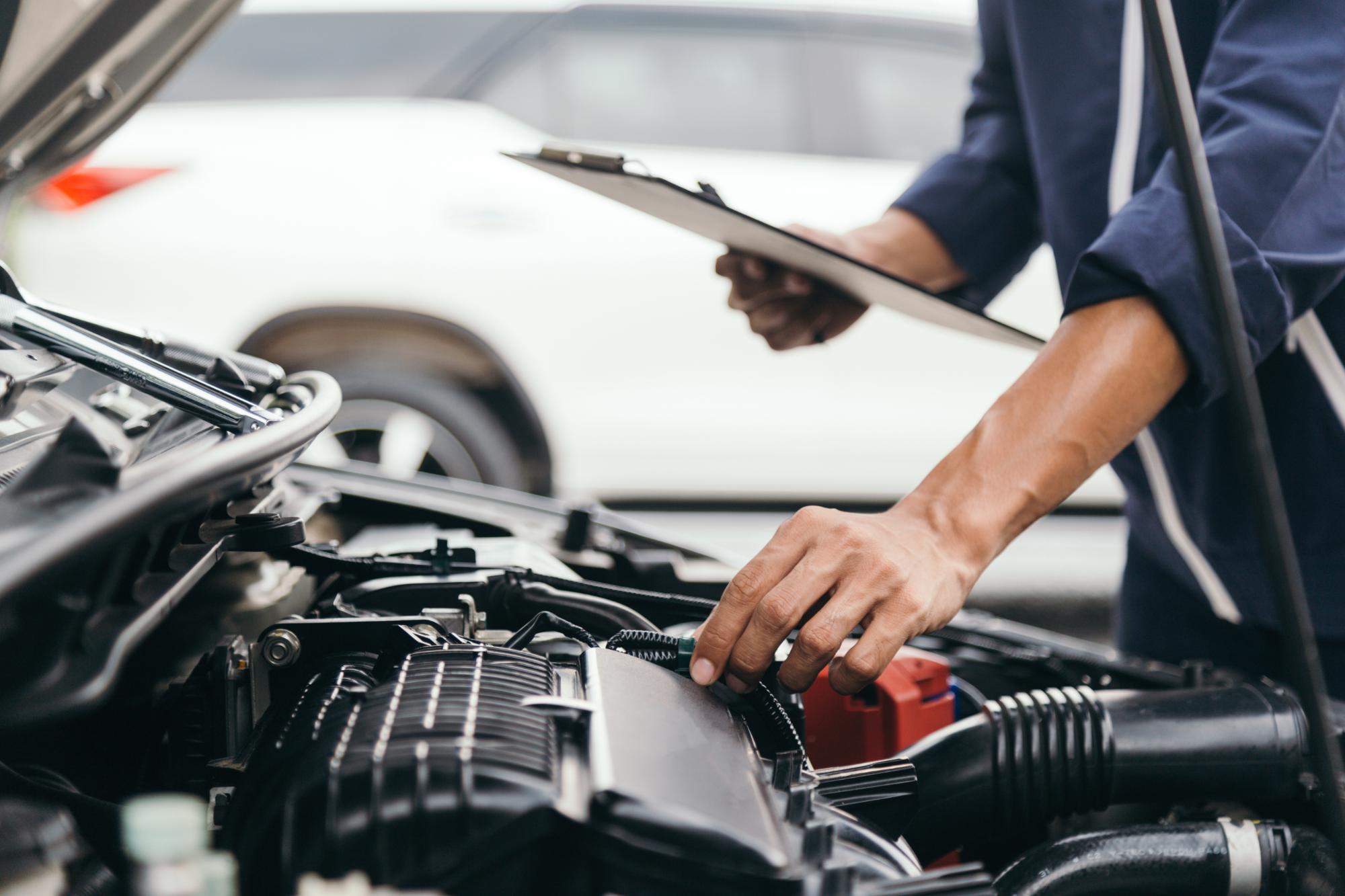 クリップボードを持った整備士が車のエンジンルームを詳しく診断している場面
