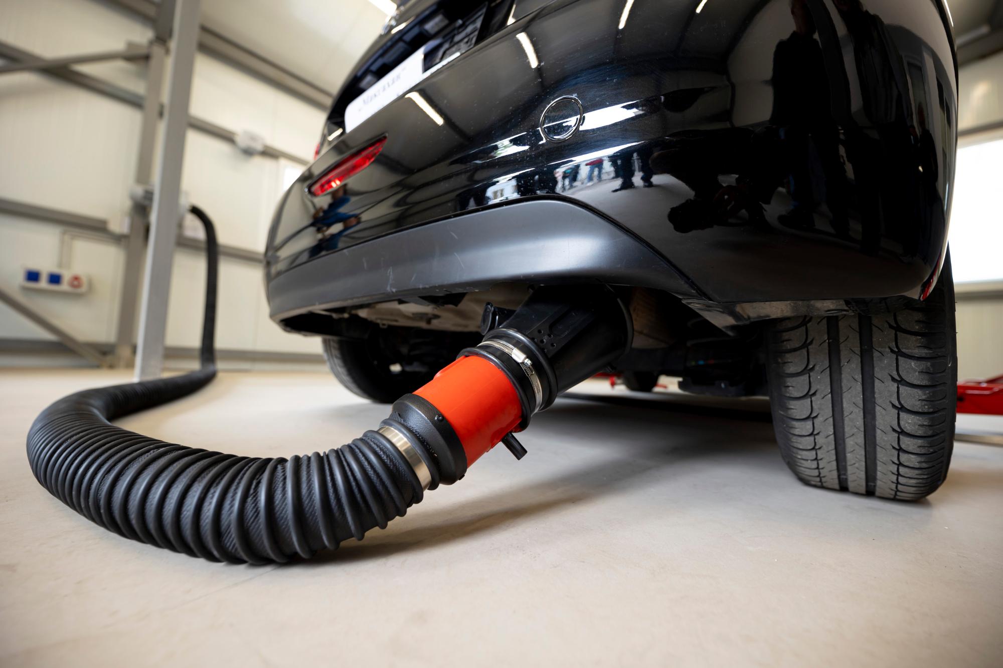 自動車の排気口に接続された黒いフレキシブルホースと赤いアダプターによる排ガス検査