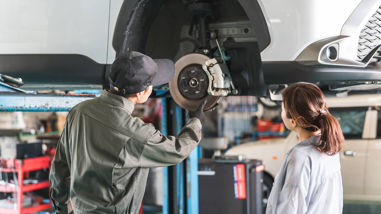 自動車整備工場でブレーキ交換の説明を受ける女性オーナーと作業着の整備士