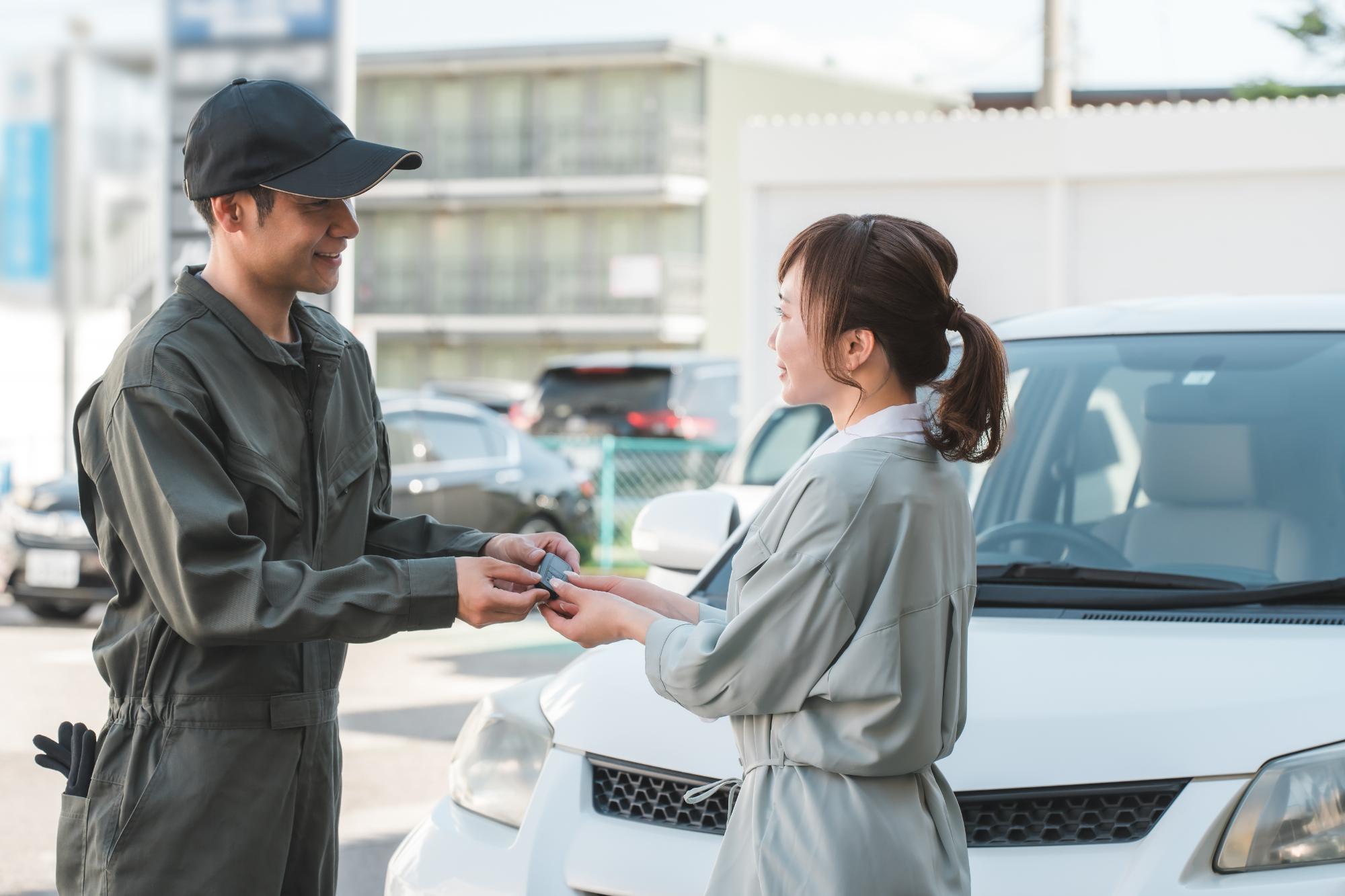 カーサービスで整備士と女性顧客が笑顔で車のキーをやり取りしている場面