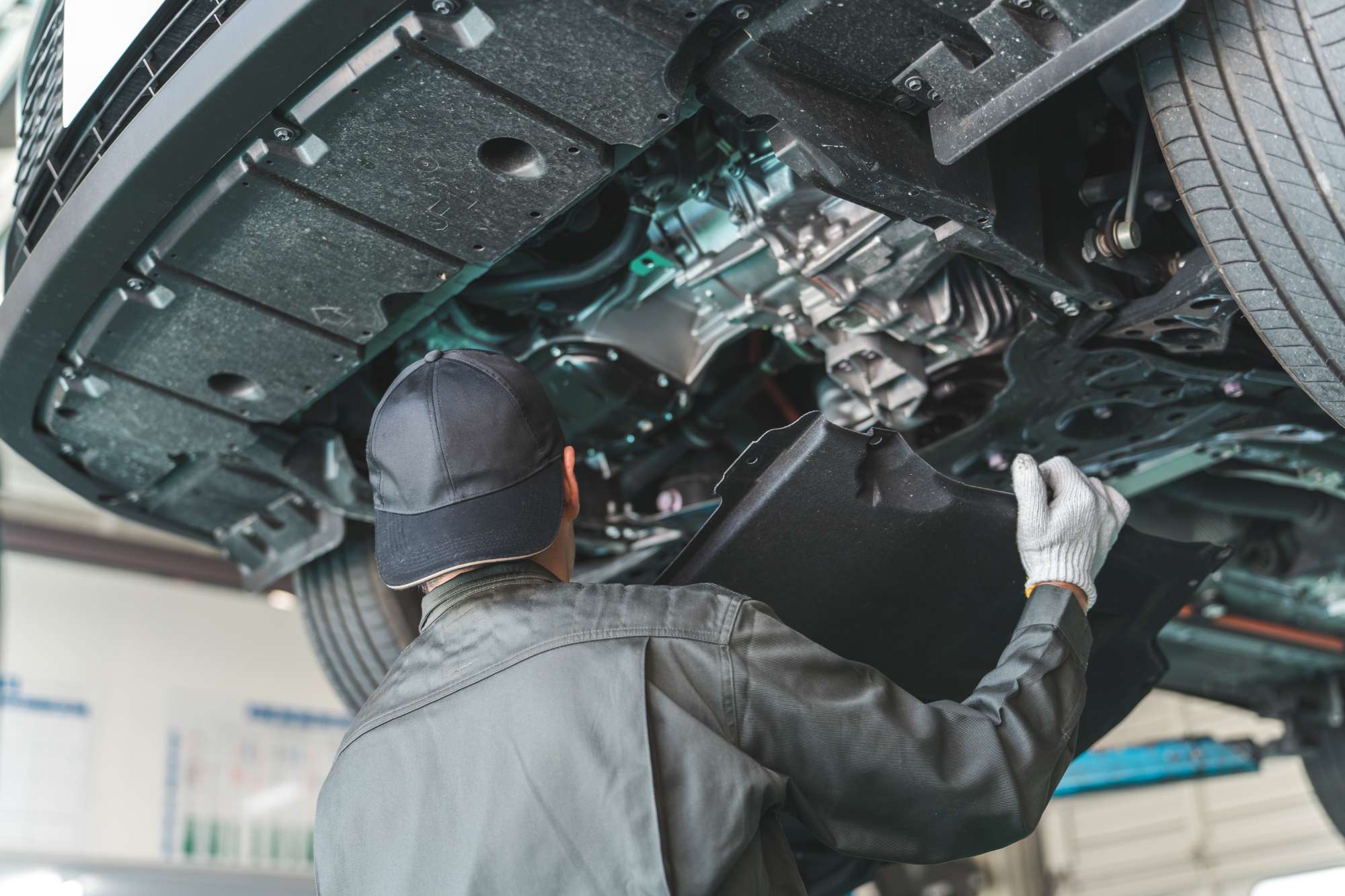 自動車整備工場でリフトアップされた車の下から足回りを確認する整備士