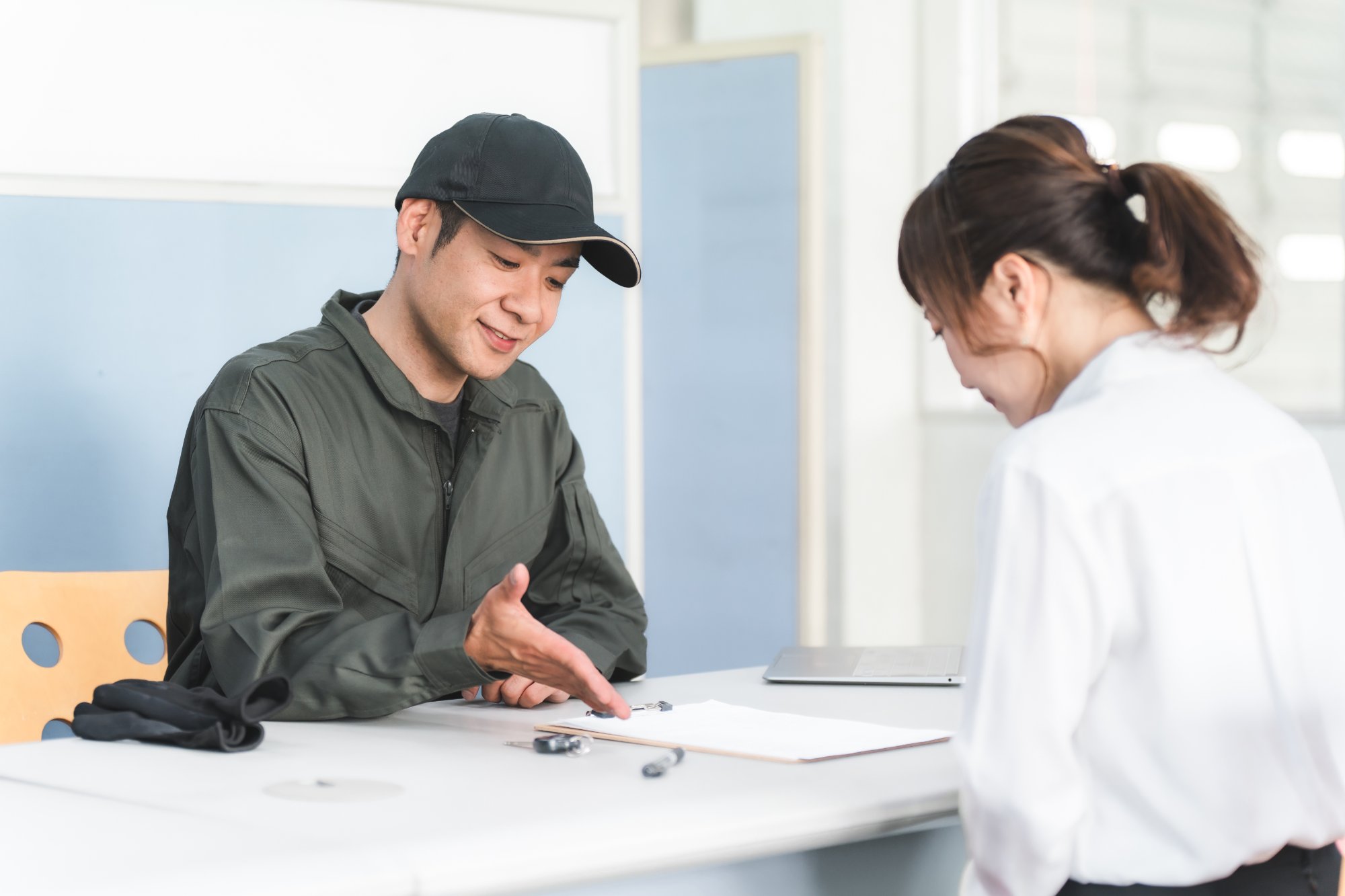 作業着を着た男性がクリップボードの書類を女性に説明している様子