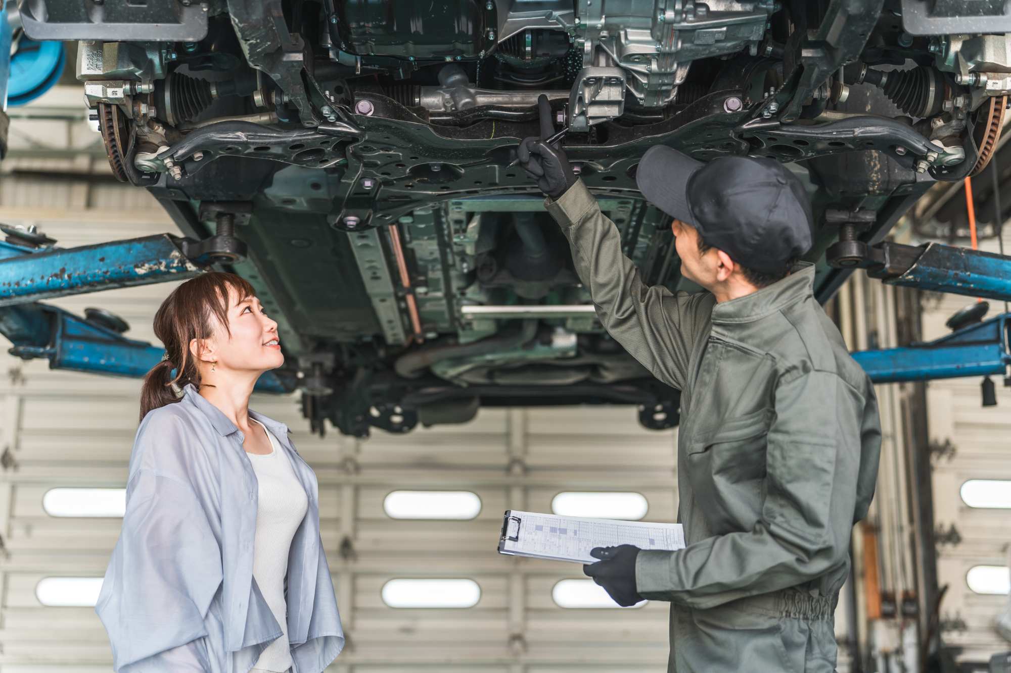 整備士が車の下回りを指差して女性客に説明している様子