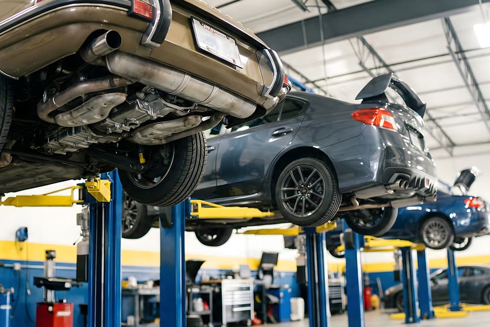 プロの整備工場でクラシックカーと現代の車がリフトアップされて整備されている場面