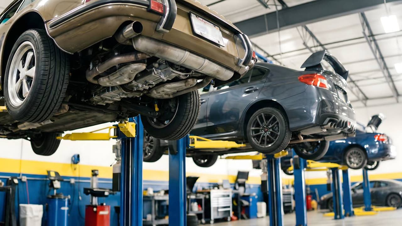プロの整備工場でクラシックカーと現代の車がリフトアップされて整備されている場面
