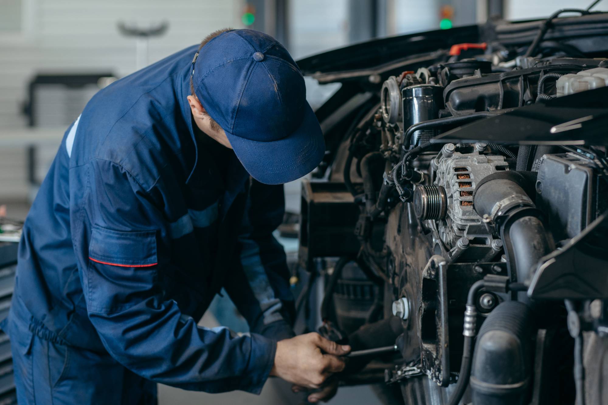 プロの整備士がガレージで車のエンジンにレンチを使って作業している場面