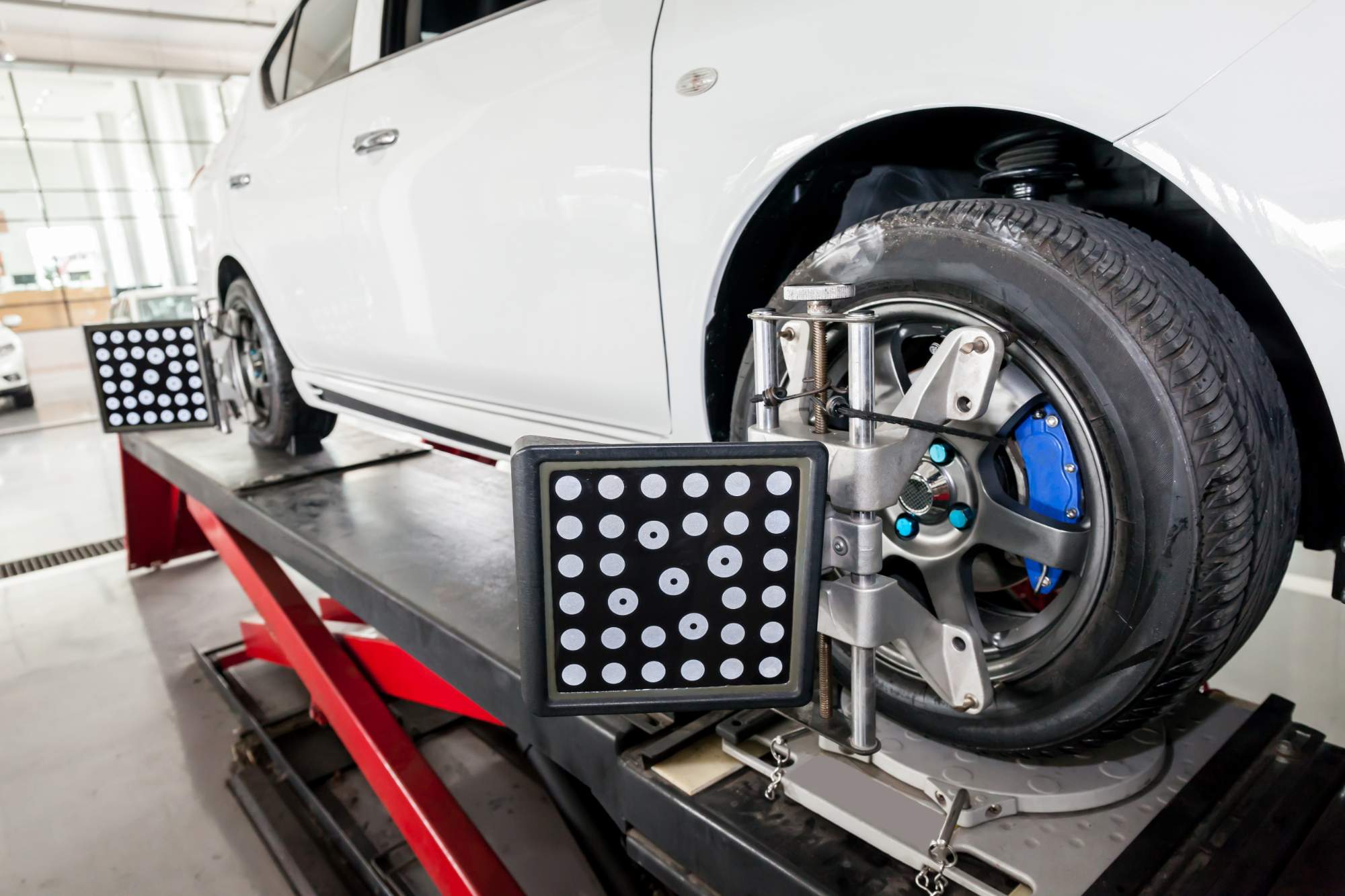 自動車整備工場でホイールアライメント測定器を取り付けた白い車のタイヤ